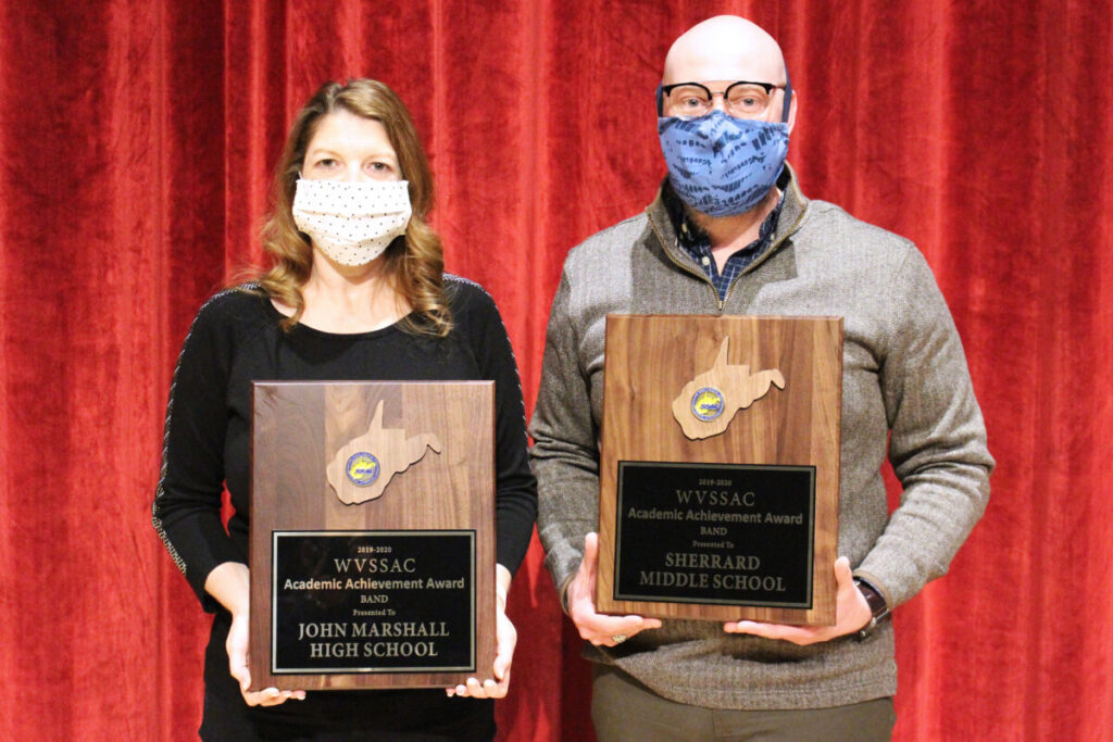Pictured from left: JM Band Director Tracey Filben and SMS Band Director Jason Burch display their schools’ award. They are standing in front of a red stage curtain.