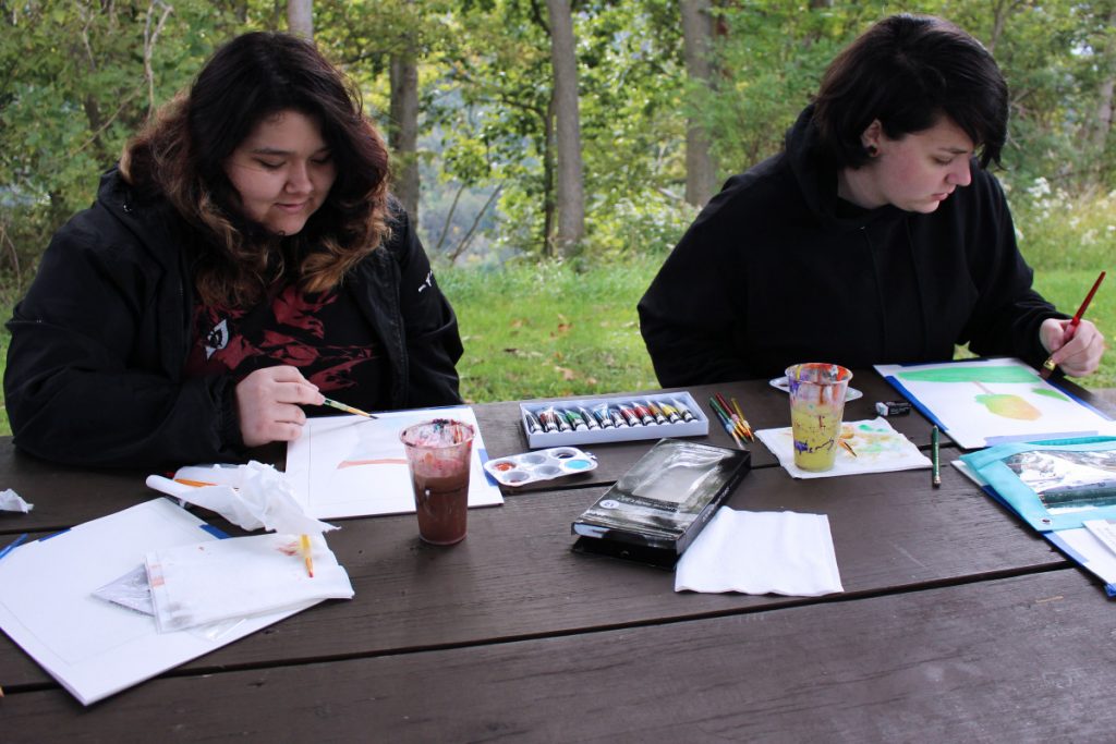 Pictured from left: JMHS junior Jenna McDaniel and JMHS sophomore Shyanna Reynolds use the Grand Vue Park landscape as inspiration for their paintings.